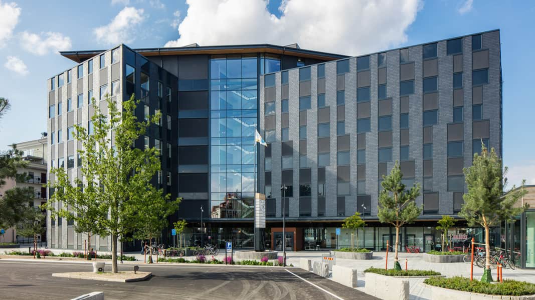 Bild på hur fastigheten ser ut, mörkt grå fasad med glaspartier där det är trapphus.