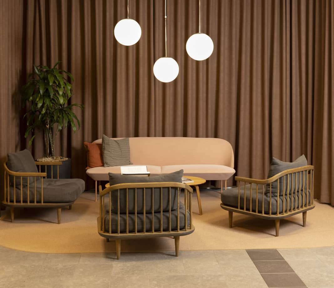 Soffa i rosa och fåtöljer i trä och grått som står framför en vägg med ett brunt hängande tygstycke