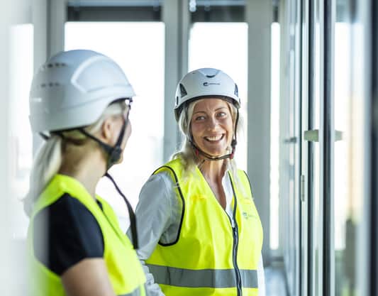 Två personer i varselkläder står vid ett fönster.