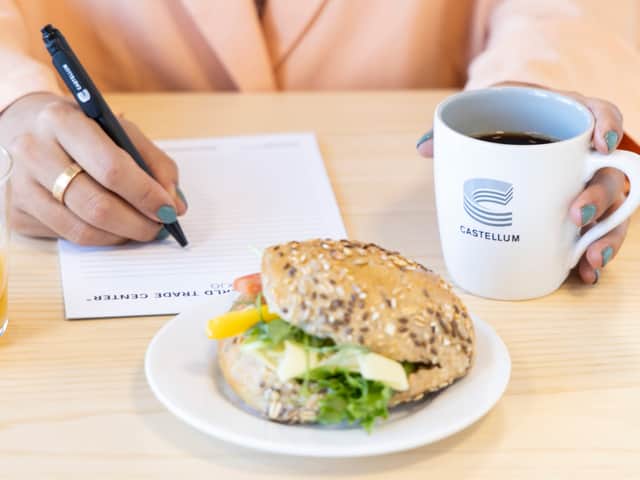 Castellum kaffekopp med fralla och ett anteckningsblock som någon skriver på.