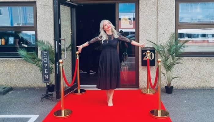 En kvinna står på en röd matta framför en byggnad.