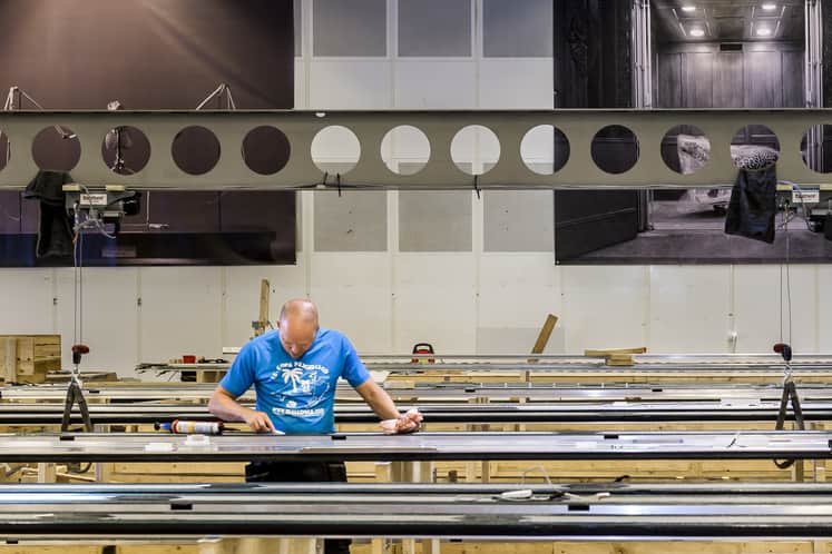 Person står och jobbar vid ett långt bord, det är högt i tak. Lagerlokal.