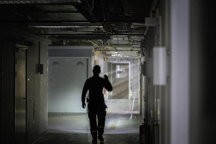 Siluett av person som lyser med ficklampa i en mörk källargång