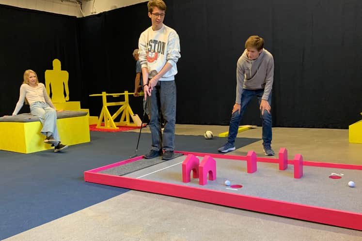 Tre ungdomar som spelar ett spel med klubba och boll inomhus i Bollkampens lokaler.