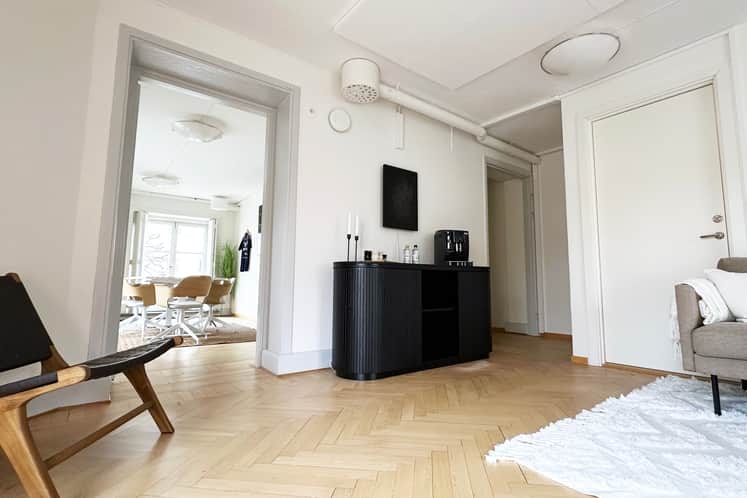 Rum med ljus fiskbensparkett, svart sideboard, högt i tak.