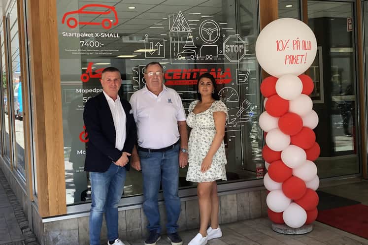 Tre personer står vid entrén till trafikskolan.