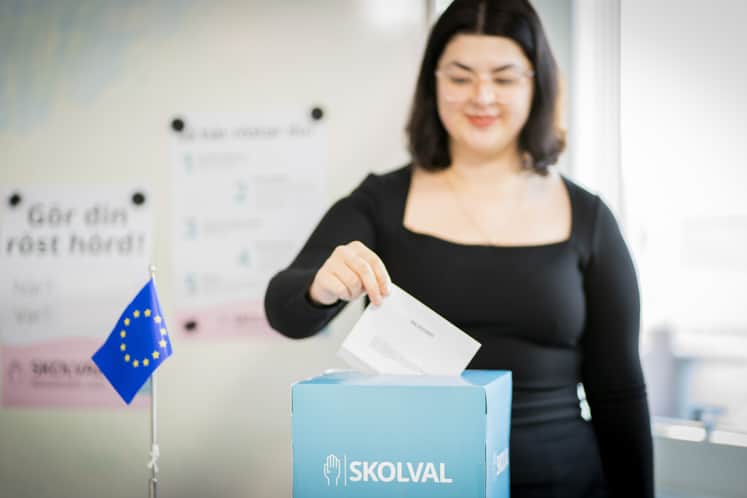 Mörkhårig ung tjej håller en valsedel i sin hand som hon är på väg att lägga i en låda för skolvalet