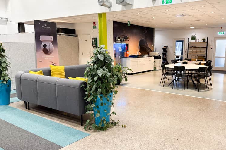 Lokal med grå soffa, gröna golvväxter och längst bort i bild ett matbord med stolar