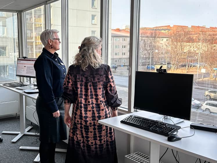 Två personer står och tittar ut genom stora fönster