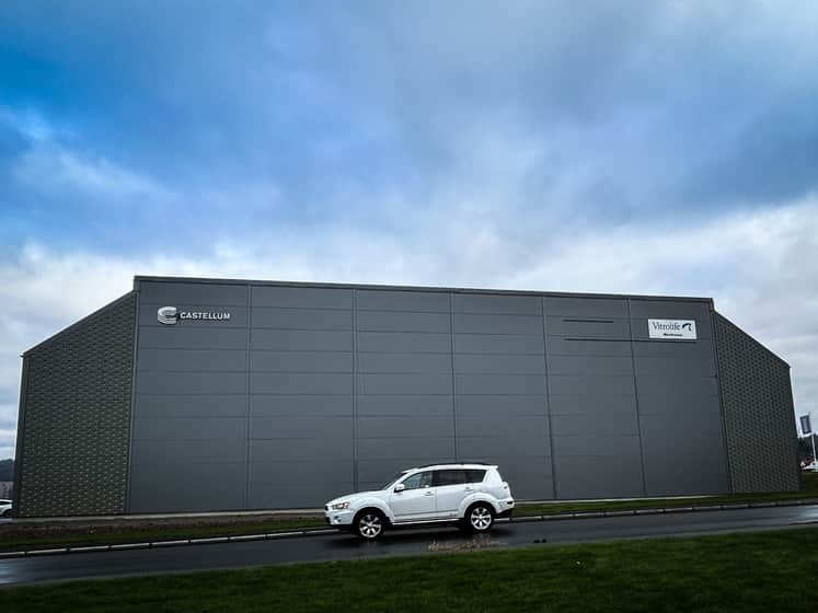 En diskret fasad i mörk ton. En ljus bil står parkerad utanför. 