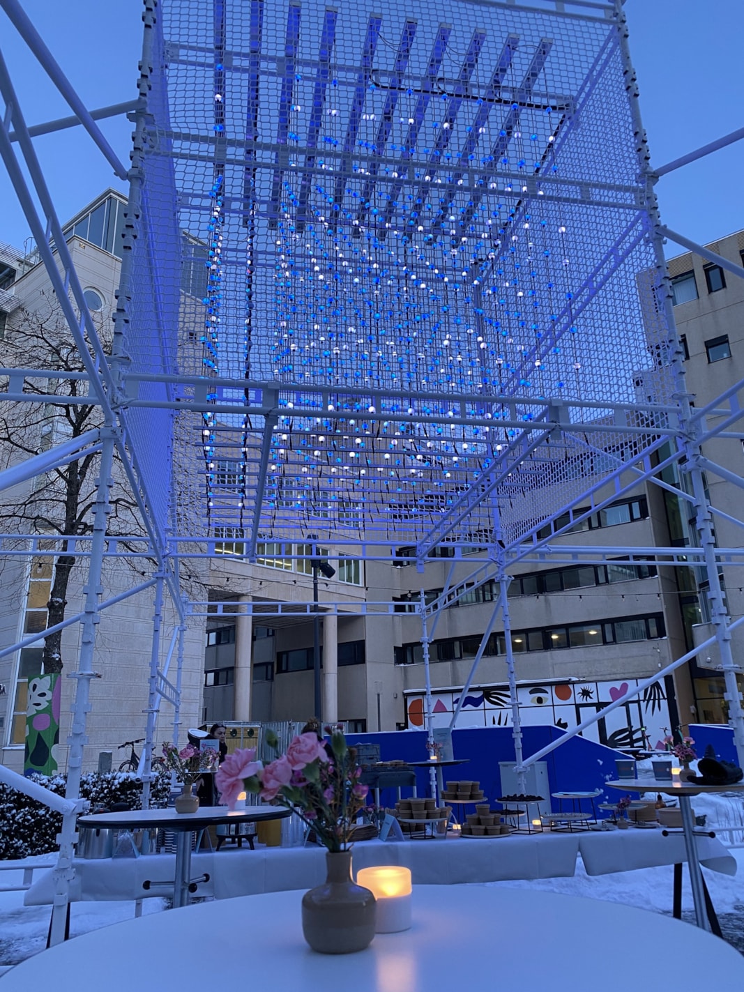 Ljusinstallation på byggställning med blomma i vas i förgrunden