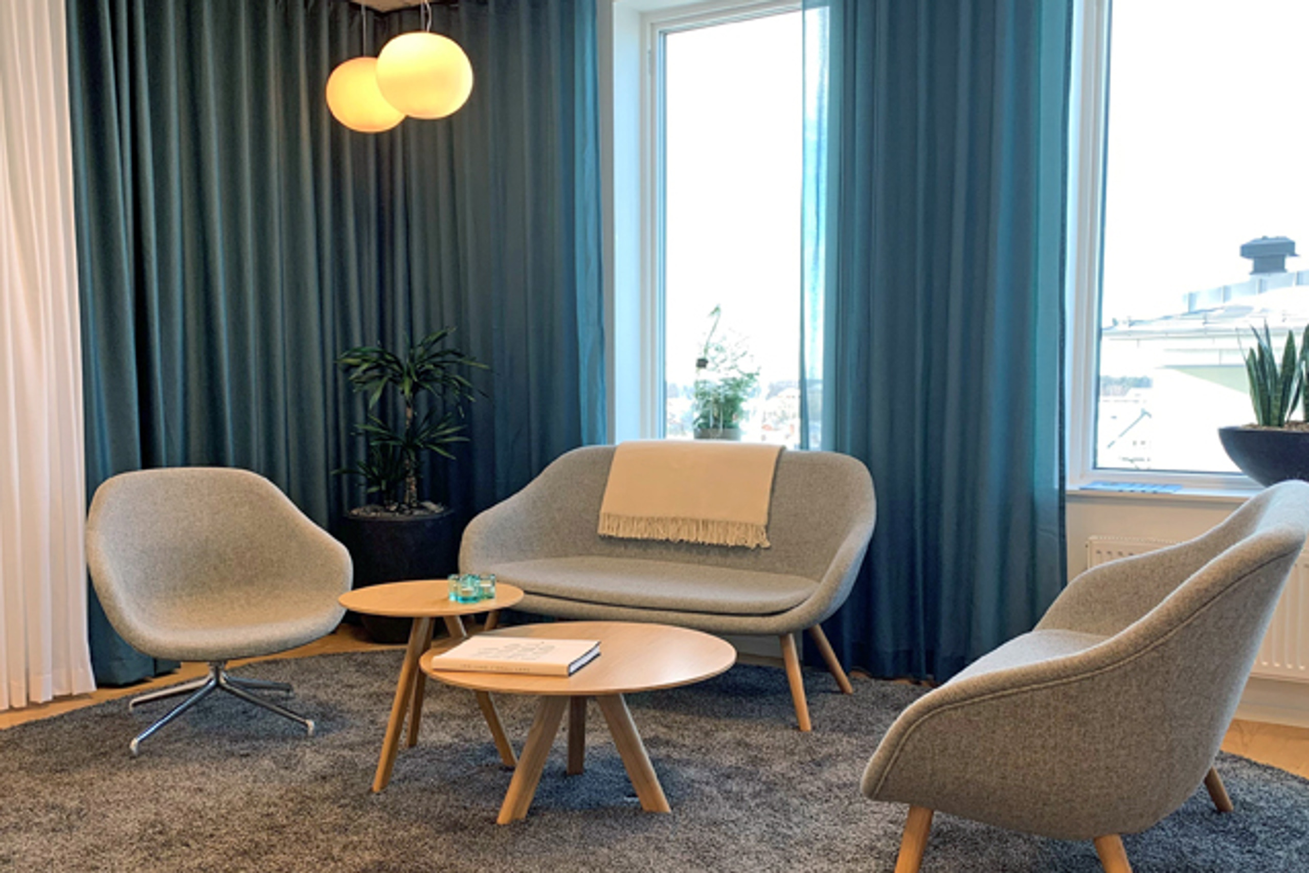 Grå soffgrupp framför fönster med blå gardiner.